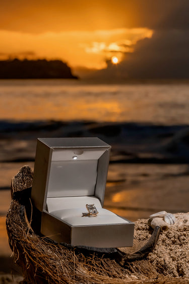 Open jewelry box with a ring on a beach at sunset